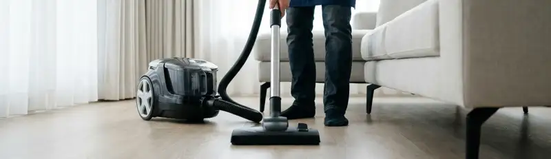 Professional house cleaner vacuuming a living room floor with a canister vacuum cleaner, Clearwater, FL.