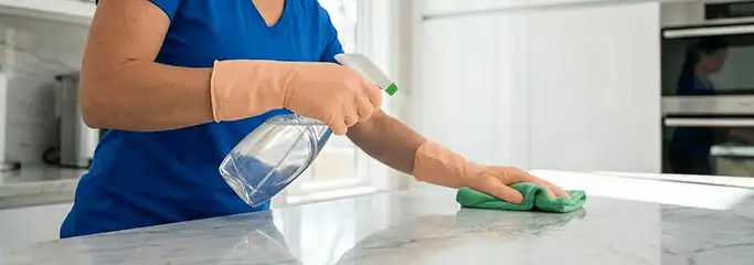 Maid service worker spraying and wiping a kitchen countertop with a microfiber cloth for sanitizing, Clearwater, FL.