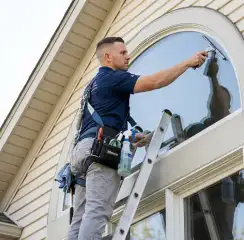 Professional window cleaner on a ladder using a squeegee to clean an exterior arched window, Clearwater, FL.