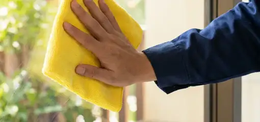 House cleaner wiping a glass window with a yellow microfiber cloth for streak-free cleaning, Clearwater, FL.